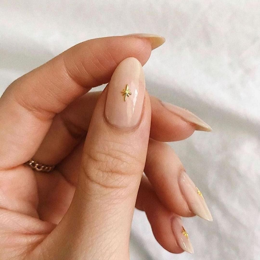 Sheer nude-pink manicure with a single small gold star charm on the thumb as the accent nail.