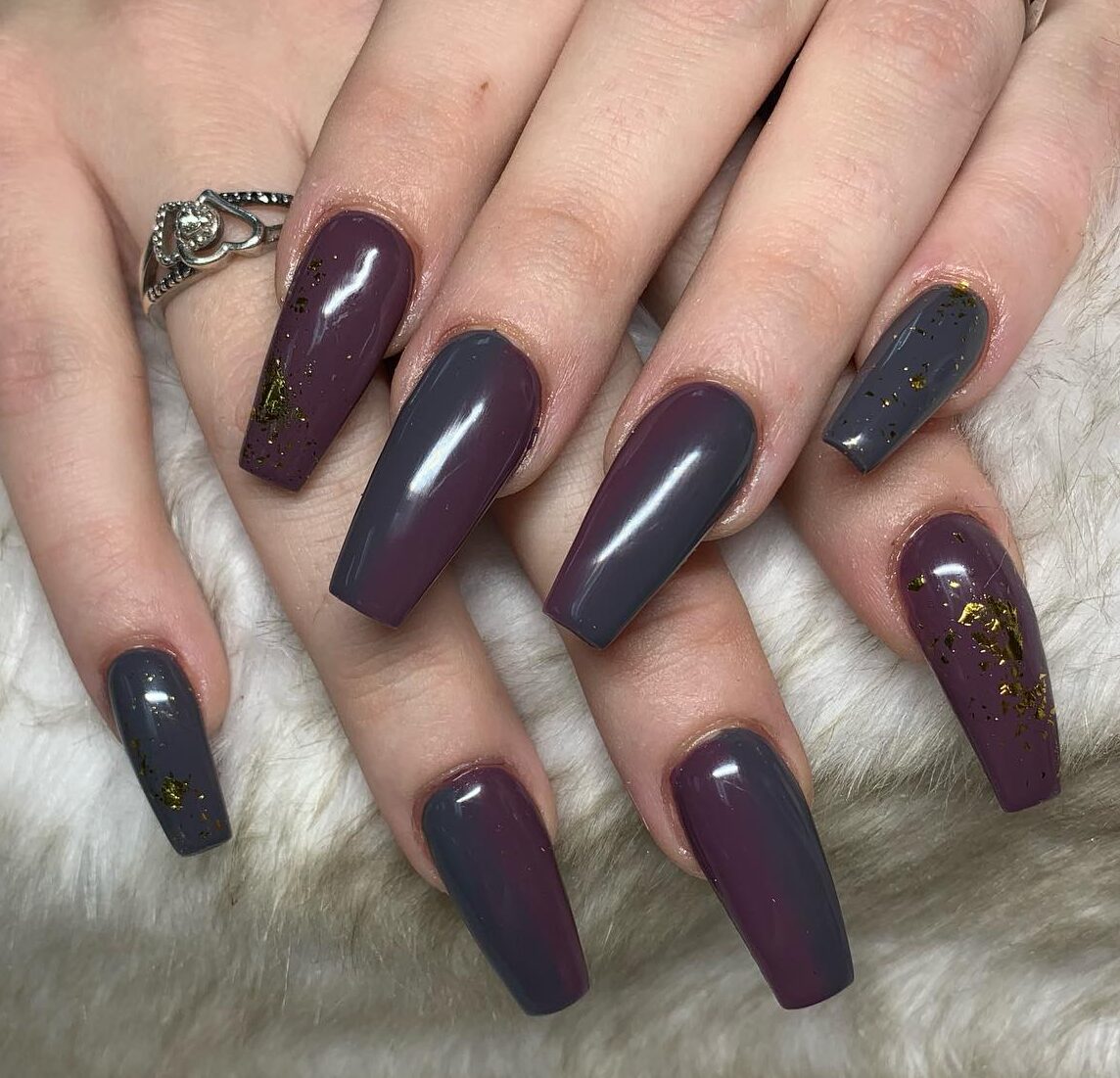 Long coffin nails in a plum-to-smoky-purple ombre with gold glitter flecks toward the tips