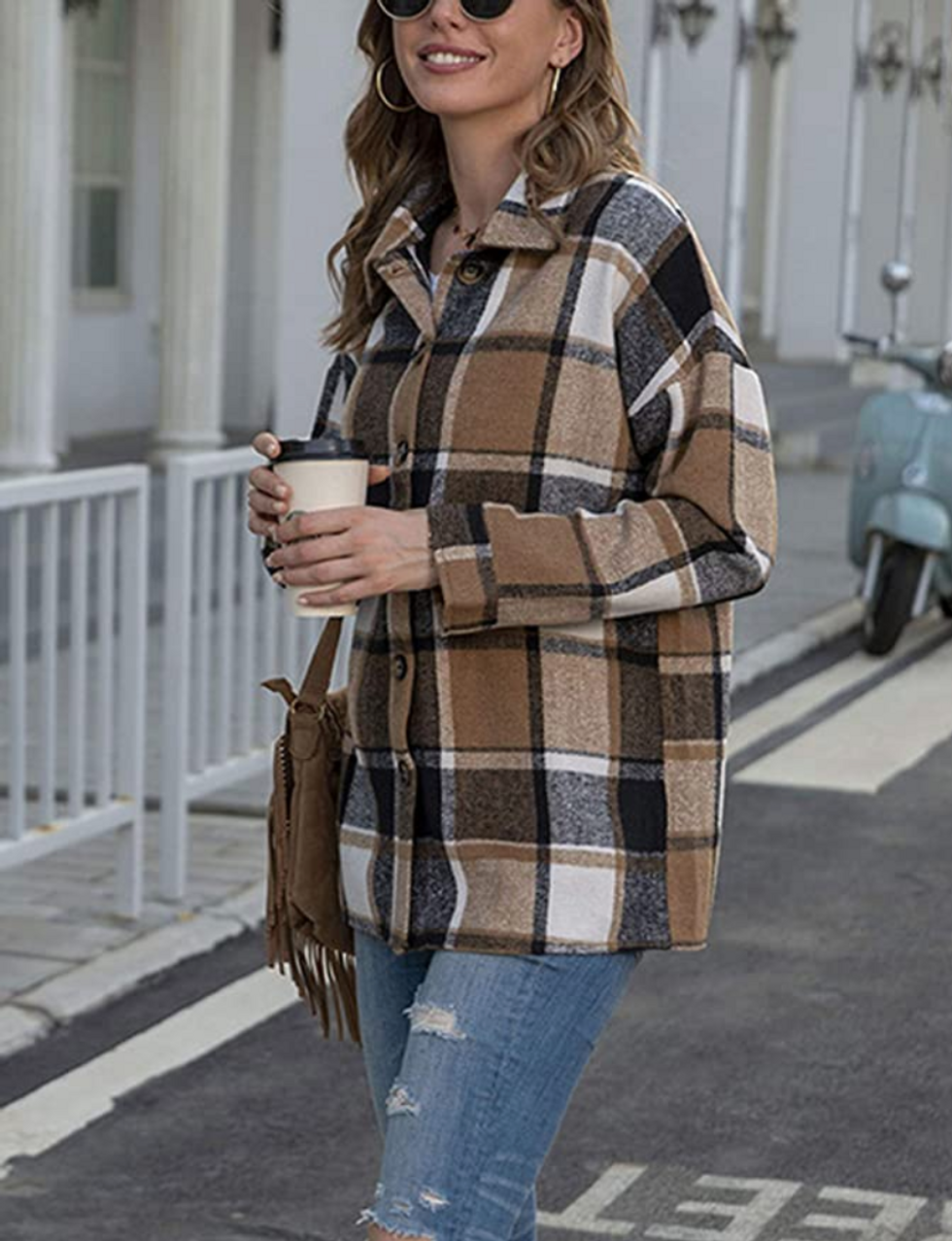 Woman wearing a brown plaid shacket with distressed jeans, a fringe bag and sunglasses