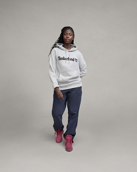 Woman in a white Timberland logo hoodie, navy cargo pants, and pink Timberland boots