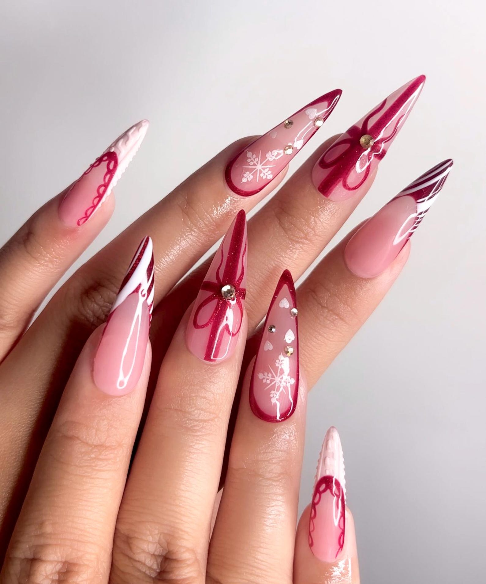 Long pink stiletto nails with red bow outlines, white snowflakes and rhinestone details