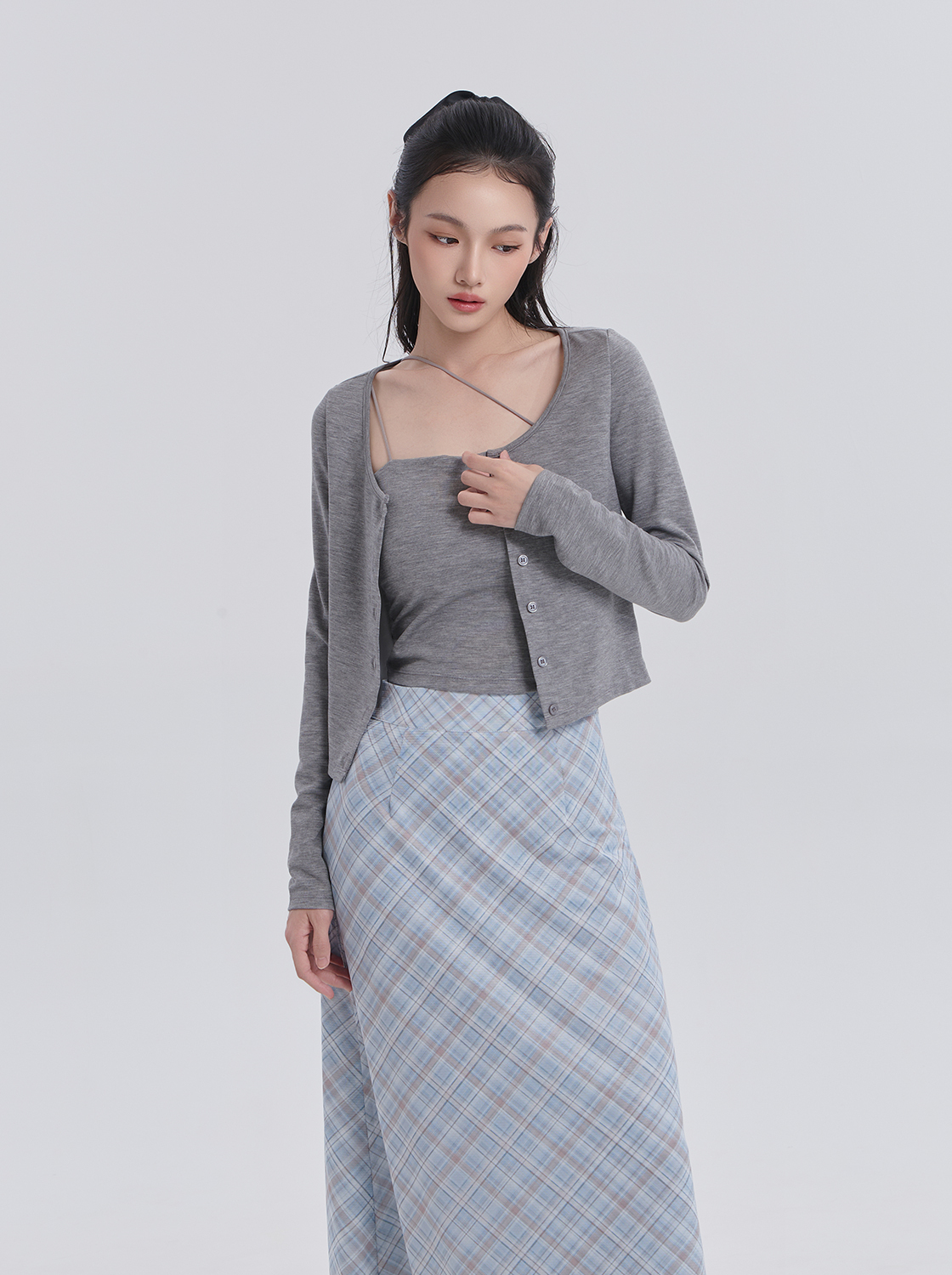 Woman wearing a grey cropped cardigan over a grey camisole with a blue plaid midi skirt