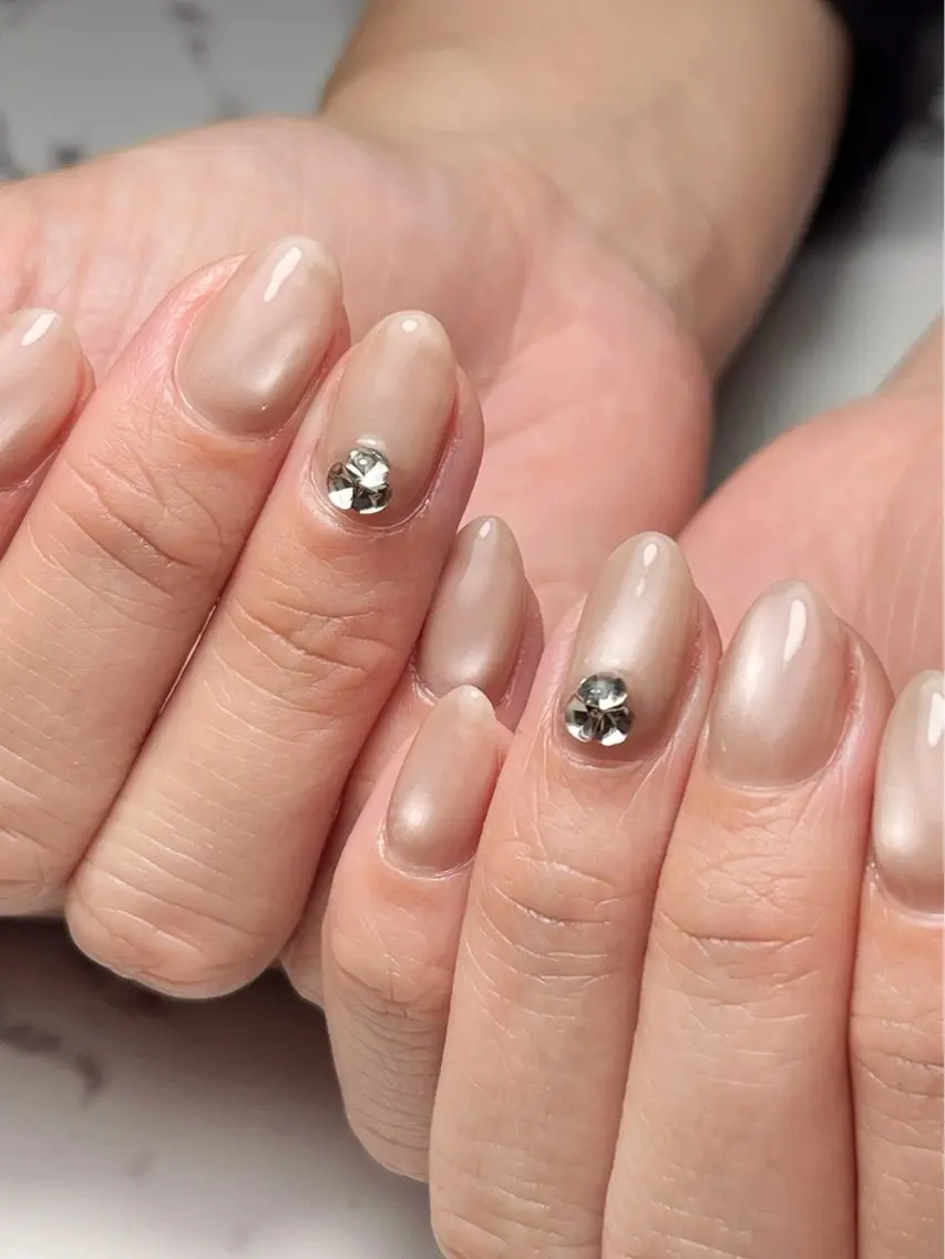 Almond nails in shimmery champagne nude with a single crystal set above the cuticle on accent nails