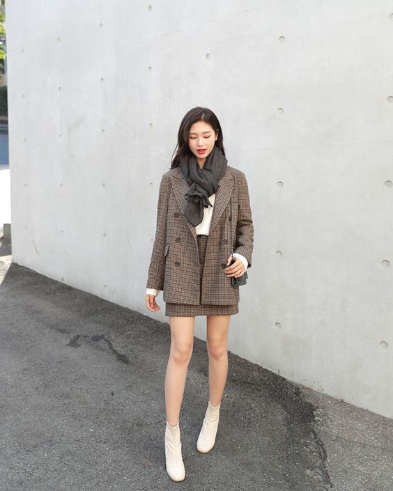 Woman wearing a plaid blazer over a brown knit dress with white ankle boots and a grey scarf