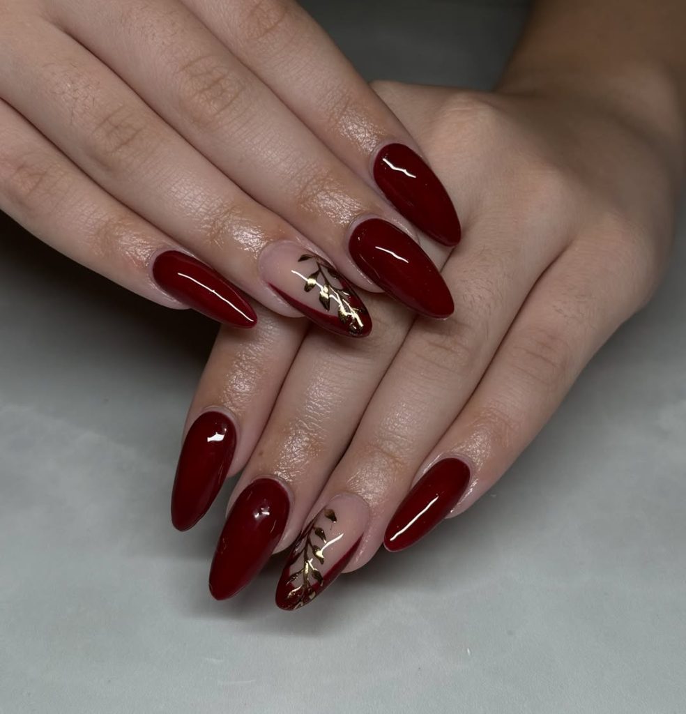 Almond deep cherry red nails with nude accent nails featuring gold leaf details