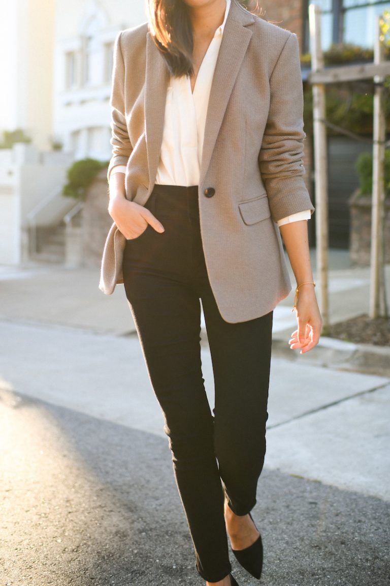 Woman outdoors wearing a taupe blazer, white silk blouse, black jeans and black pointed flats