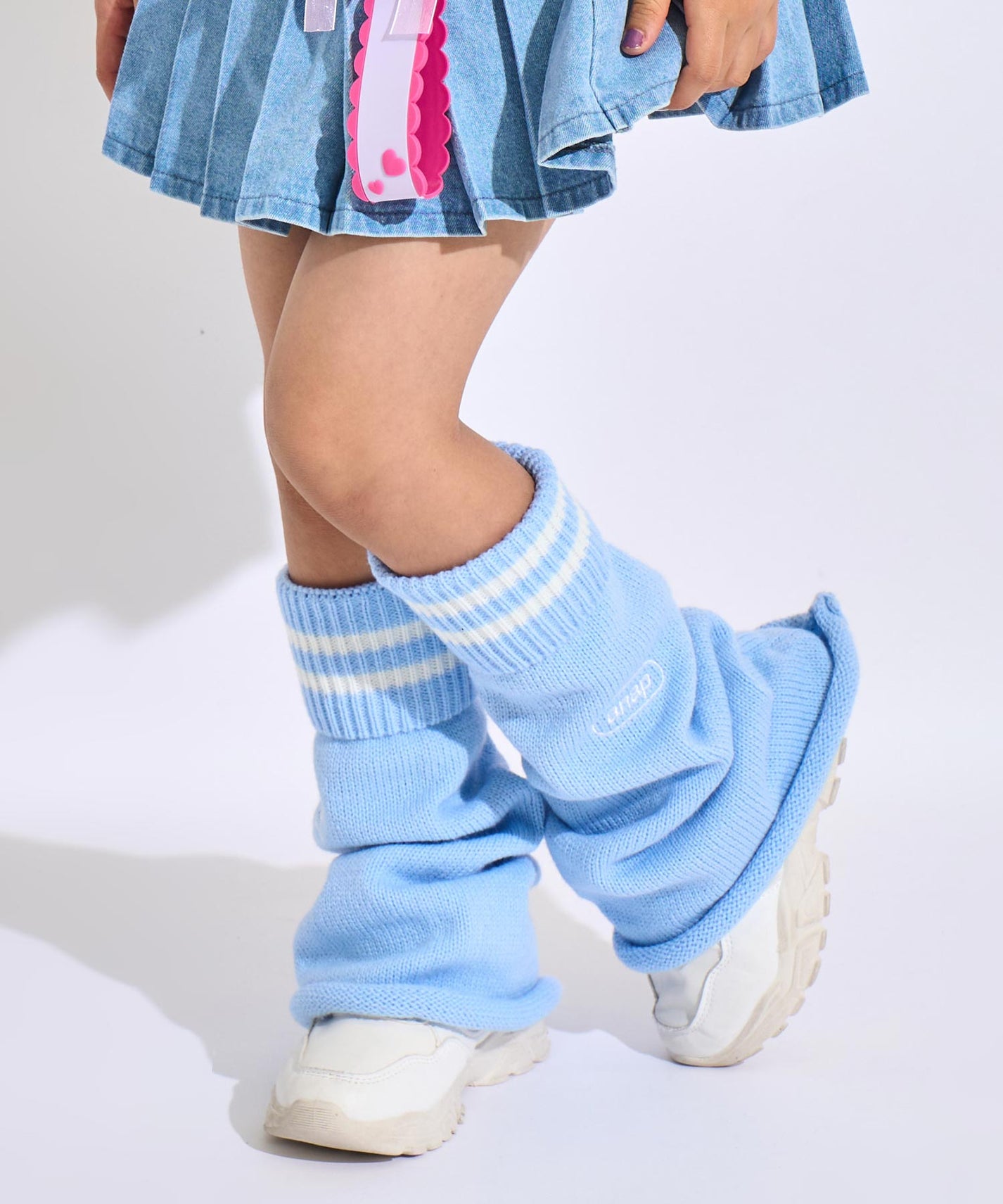 Sky blue leg warmers with white sporty stripes worn with a light denim pleated mini skirt and white sneakers