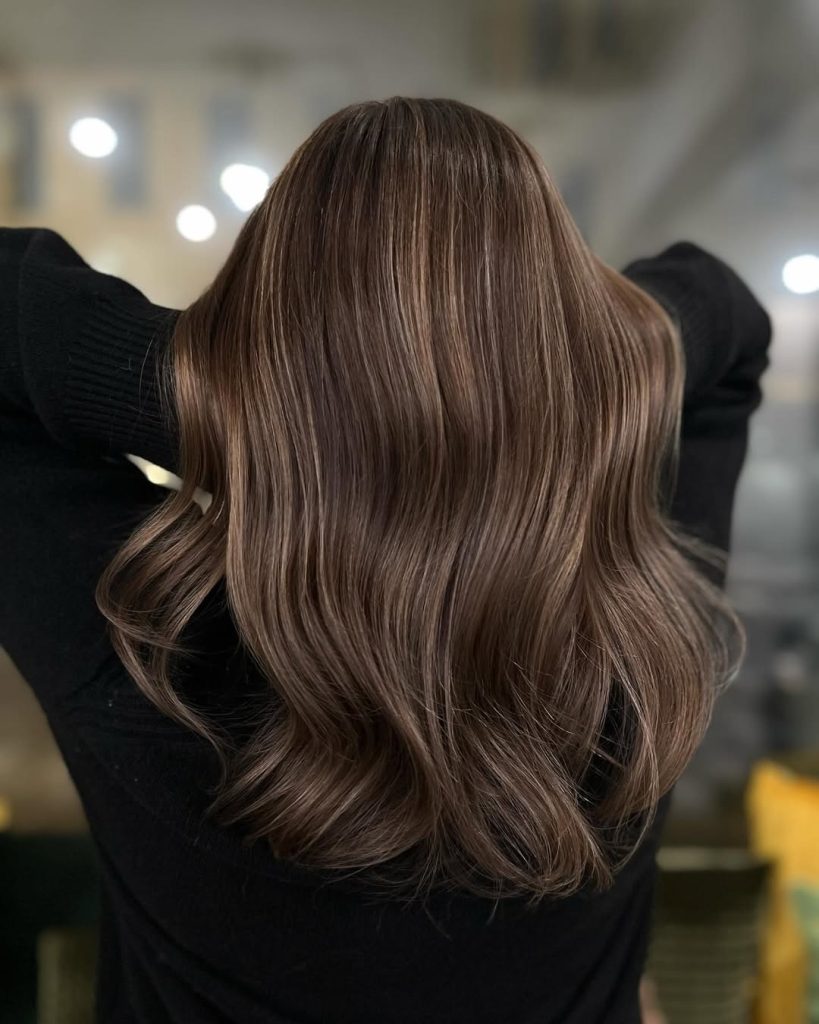 Woman with dark brown wavy hair and soft chestnut face-framing highlights