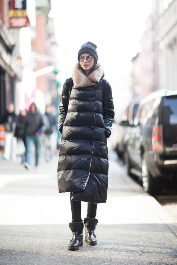 Woman in black moon boots, longline black puffer coat, black beanie and sunglasses on a city street
