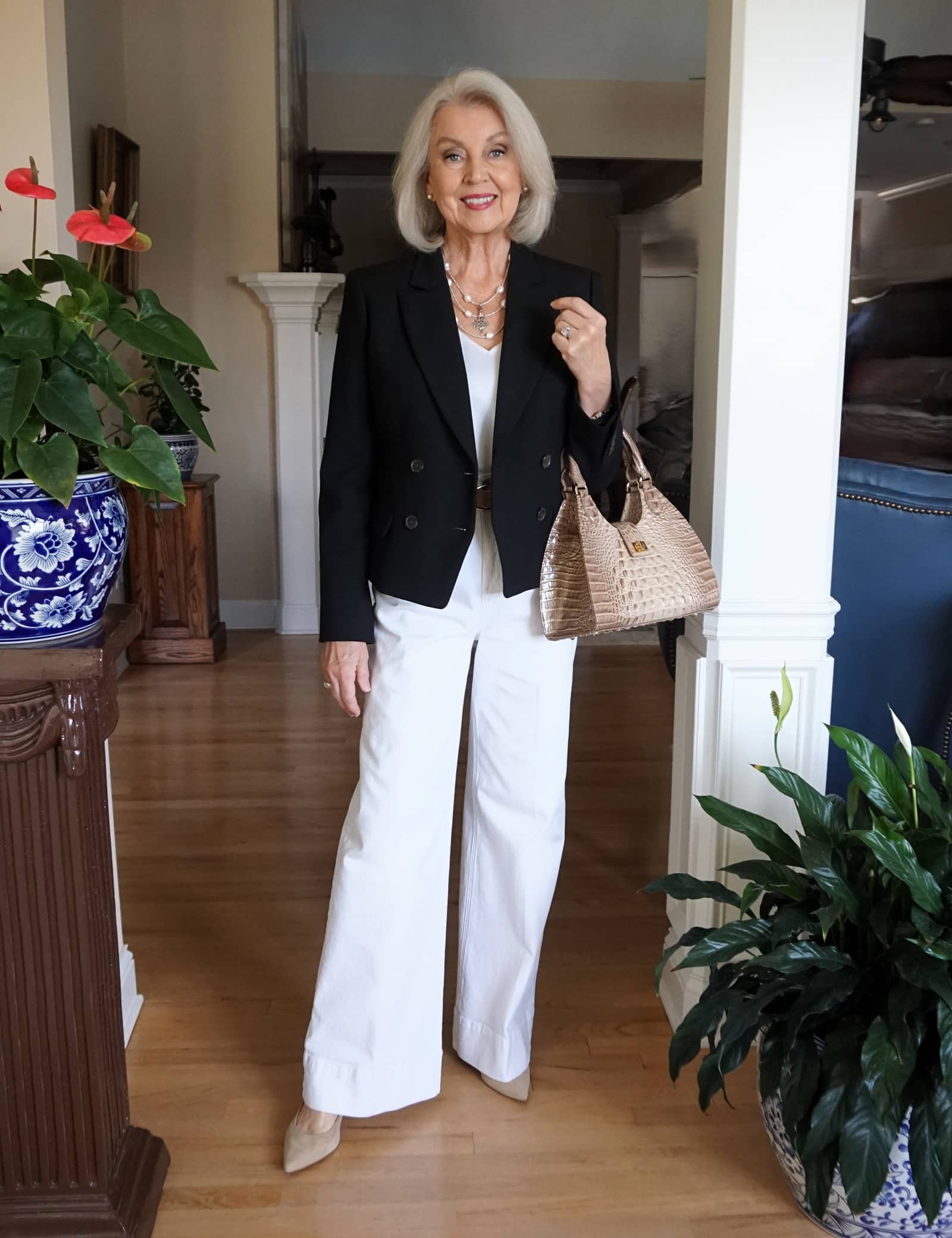 Senior woman in a black double-breasted blazer with white wide-leg trousers and layered necklaces