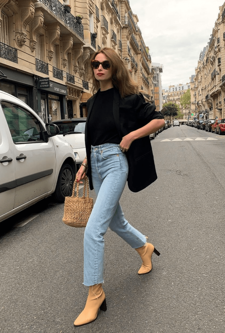 Woman in Paris wearing a black blazer, black top, light-wash jeans and tan pointed heeled ankle boots