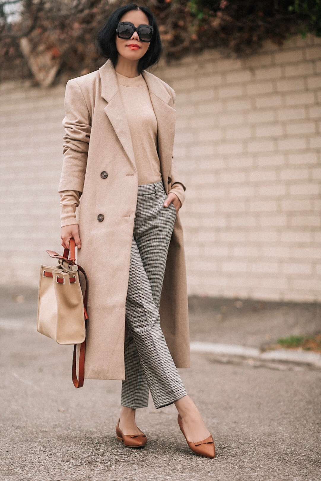 Woman wearing a camel coat over a beige knit sweater with gray plaid trousers