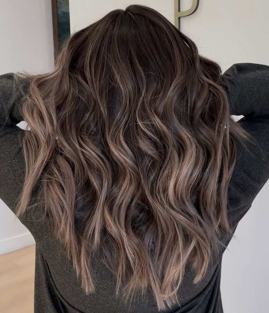 Woman with dark brunette wavy hair and cool taupe face-framing balayage highlights