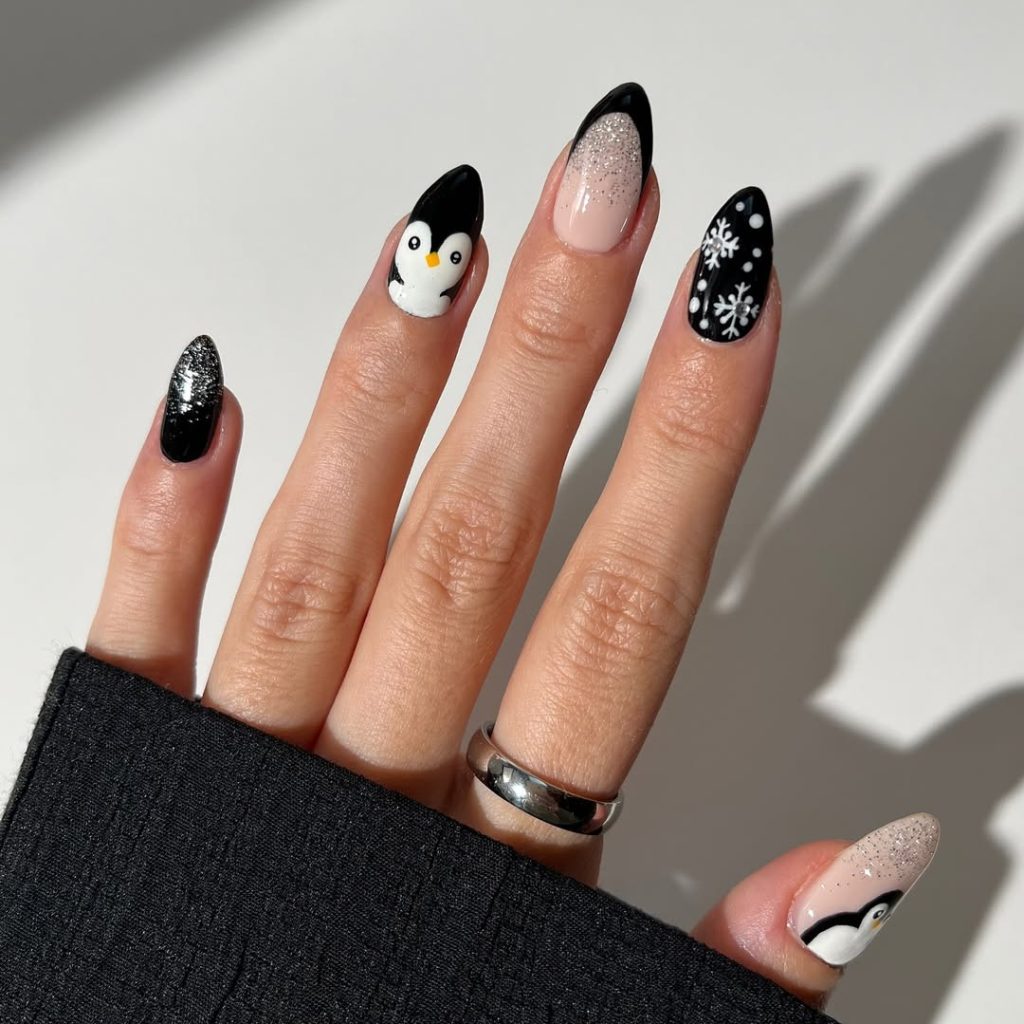 Black almond nails with painted penguin faces, silver glitter and white snowflake accents