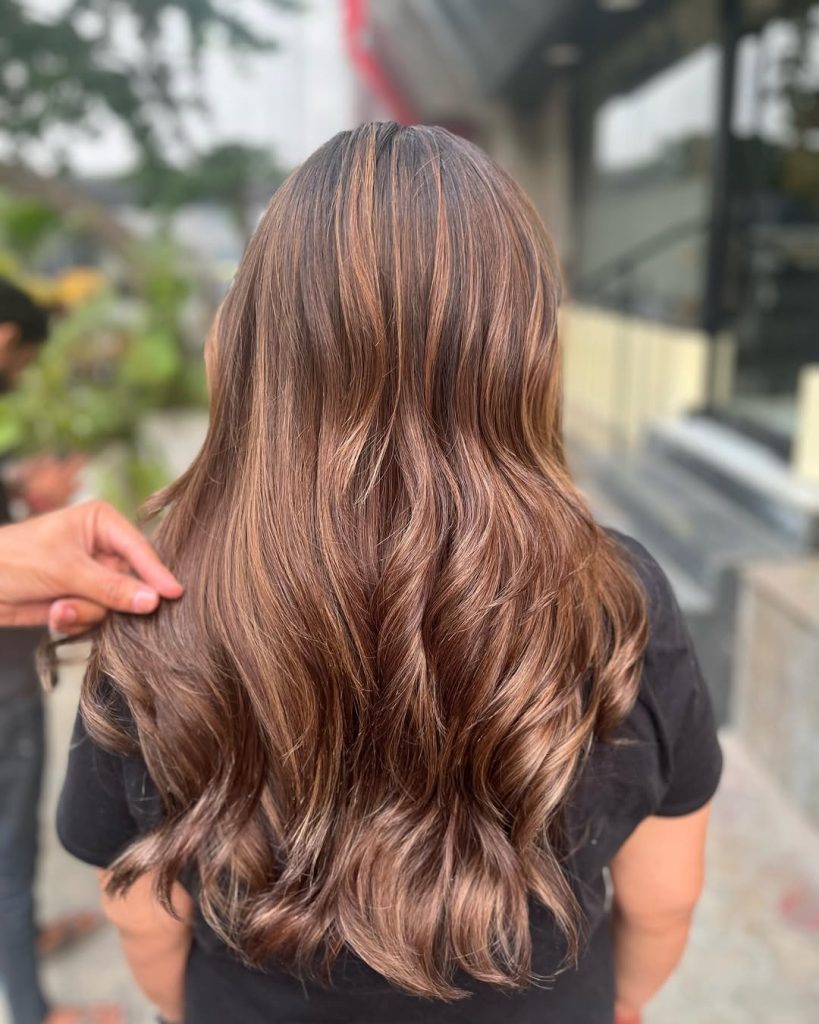 Woman with medium brown wavy hair and caramel swirl balayage money piece highlights