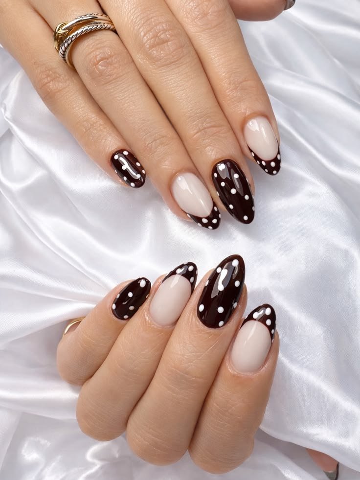 Dark chocolate-brown nails with tiny white polka dots, some with nude half-moon details.