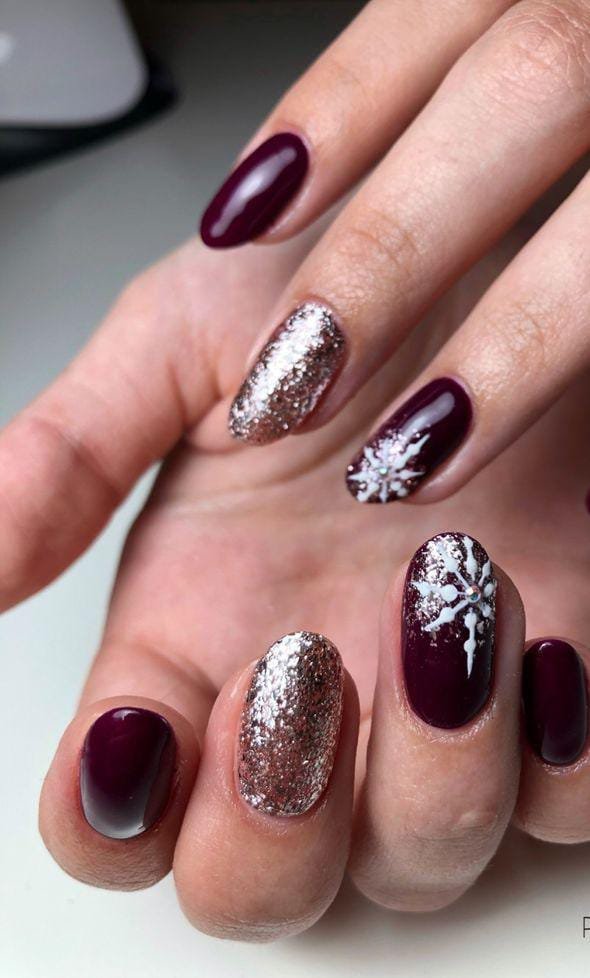 Almond nails in deep burgundy with rose-gold glitter accent nails and white snowflake nail art