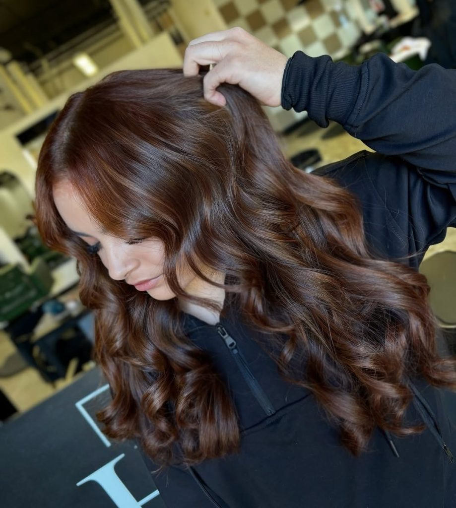 Woman with deep brunette wavy hair and warm copper money piece highlights around her face