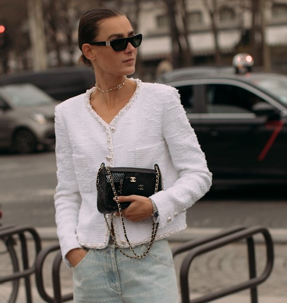 Woman in a white Chanel-style tweed jacket, light-wash jeans, sunglasses and a quilted bag on a Paris street