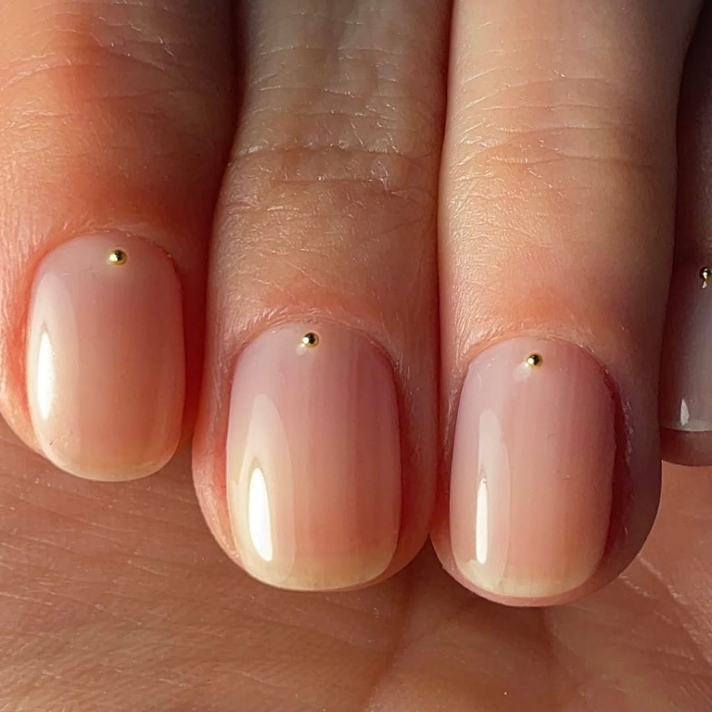 Blush nude nails with a gold dot accent at the cuticle
