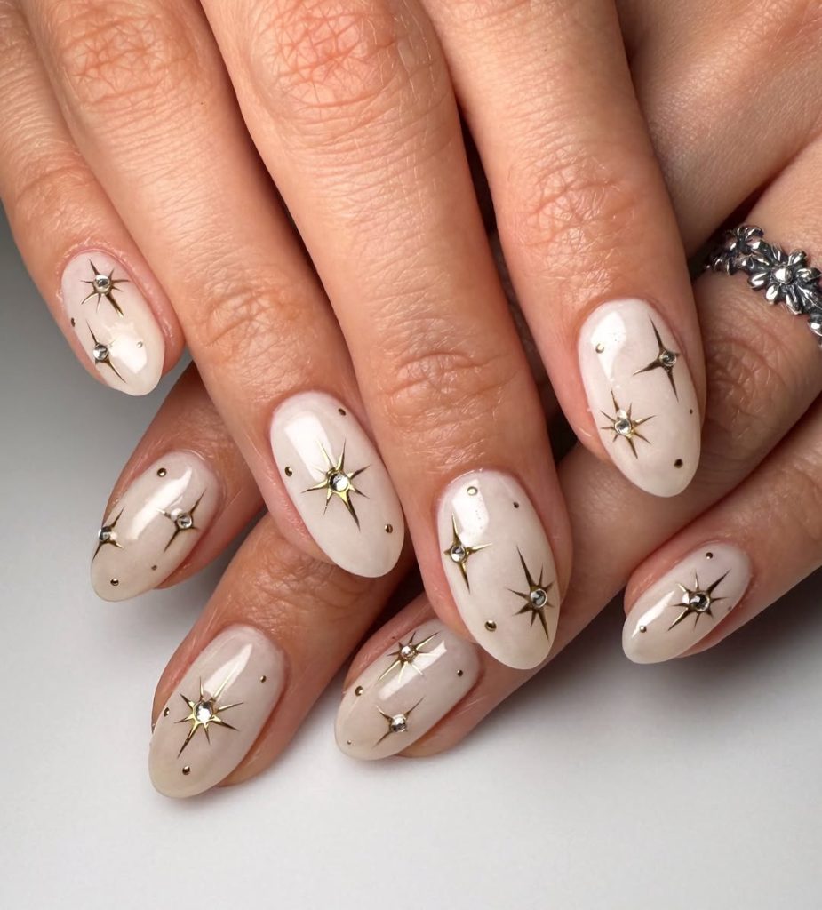 Milky white oval nails with gold starburst nail art and tiny crystals