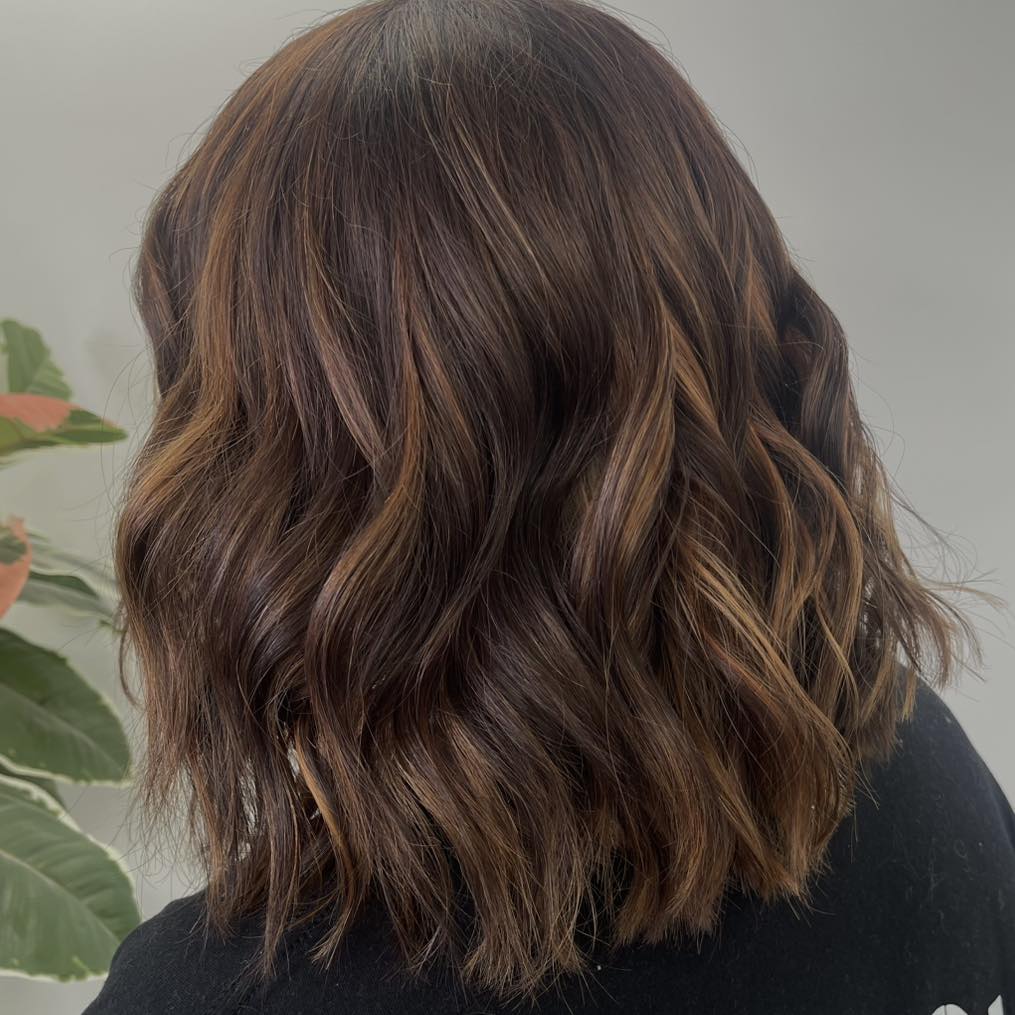 Woman with a shoulder-skimming lob and slim caramel money piece highlights around her face