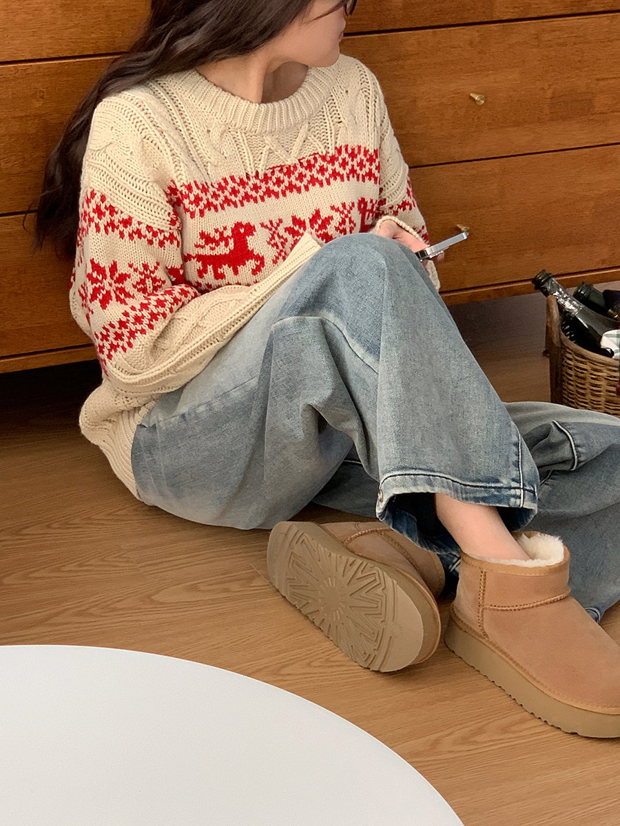 Woman in a cream fair-isle reindeer sweater with light-wash wide-leg jeans and tan shearling boots, sitting indoors