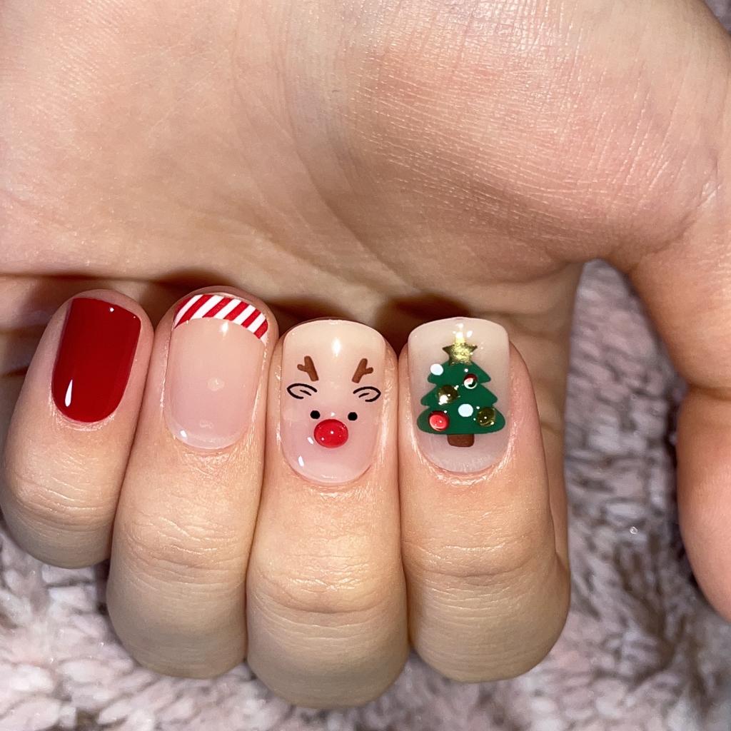 Short red and nude Christmas nails with a reindeer face, candy stripe tip and tree art
