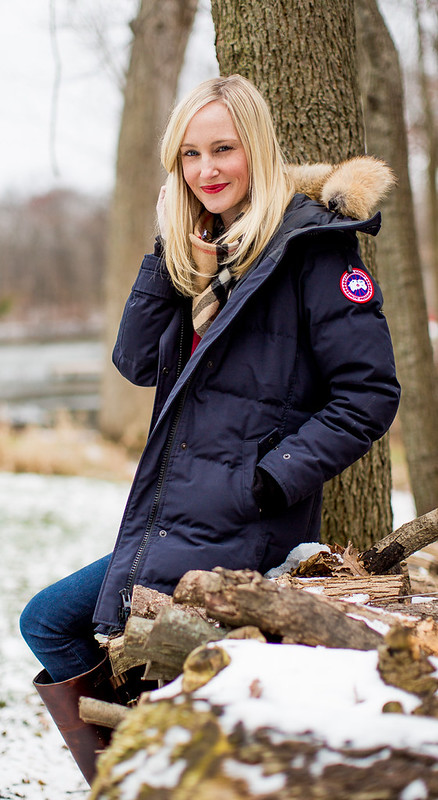 Woman in a navy fur-hood parka with a striped scarf in a snowy woodland