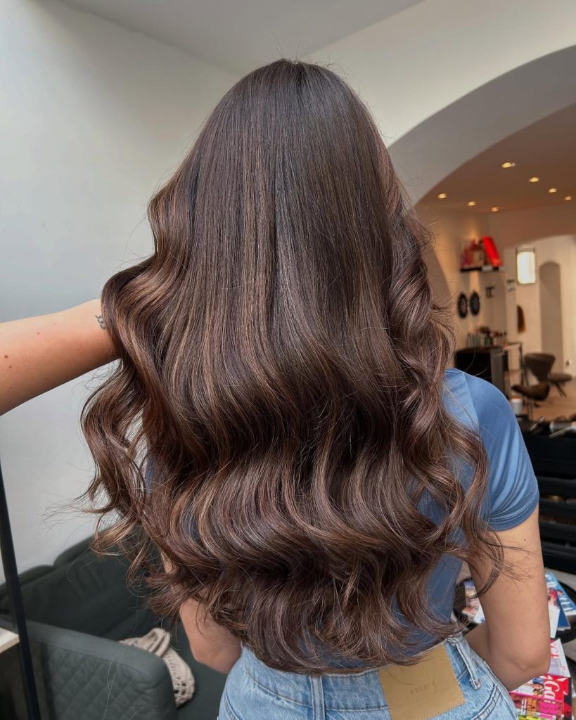 Woman with glossy chocolate-chestnut wavy hair and fine face-framing highlight slices