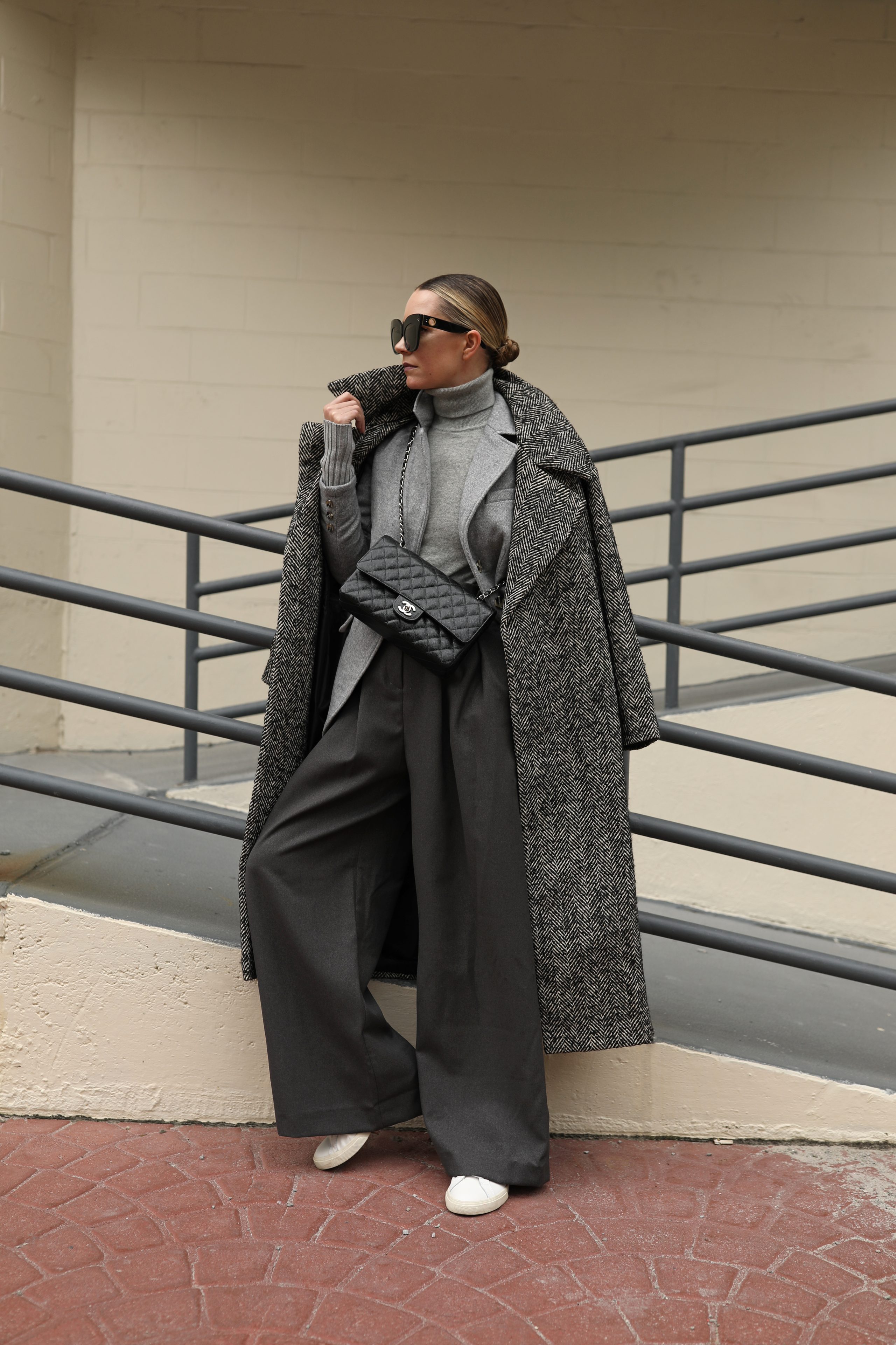 Woman wearing a herringbone overcoat over a gray turtleneck with charcoal wide-leg trousers