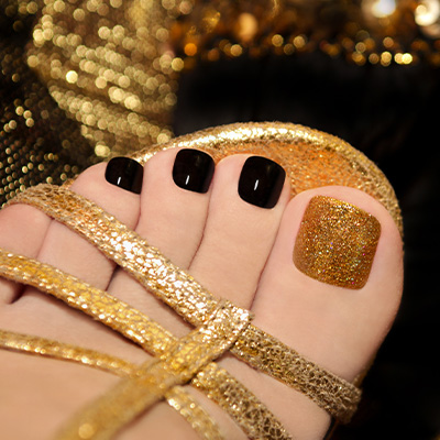 Black pedicure with a gold glitter big toe, worn with gold strappy sandals
