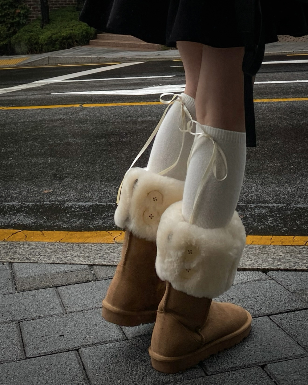White leg warmers with trailing ribbon ties worn with tan shearling cuff boots on a city street