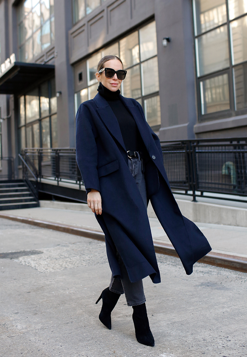 Woman in a navy wrap coat over a black turtleneck with cropped grey jeans and heeled ankle boots