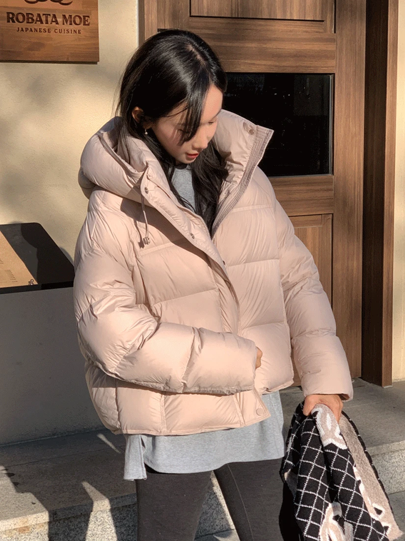 Woman wearing a beige cropped puffer jacket with a grey top and black pants