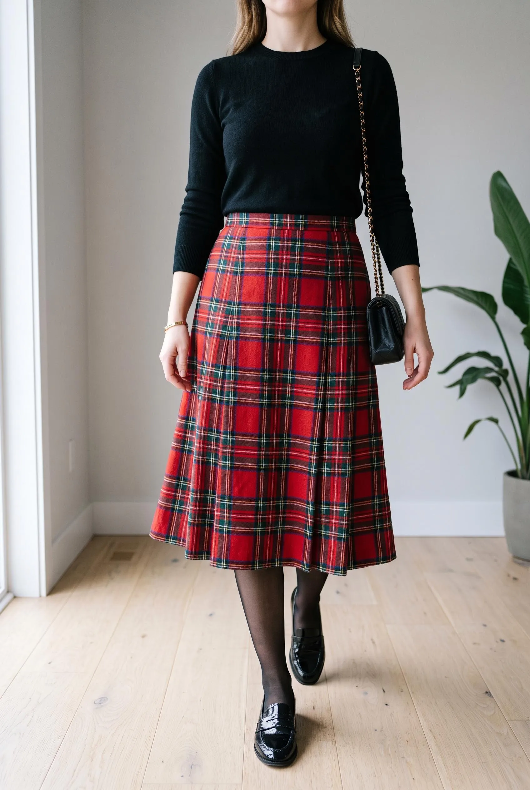 Black knit sweater with a red tartan pleated midi skirt, sheer tights and black loafers