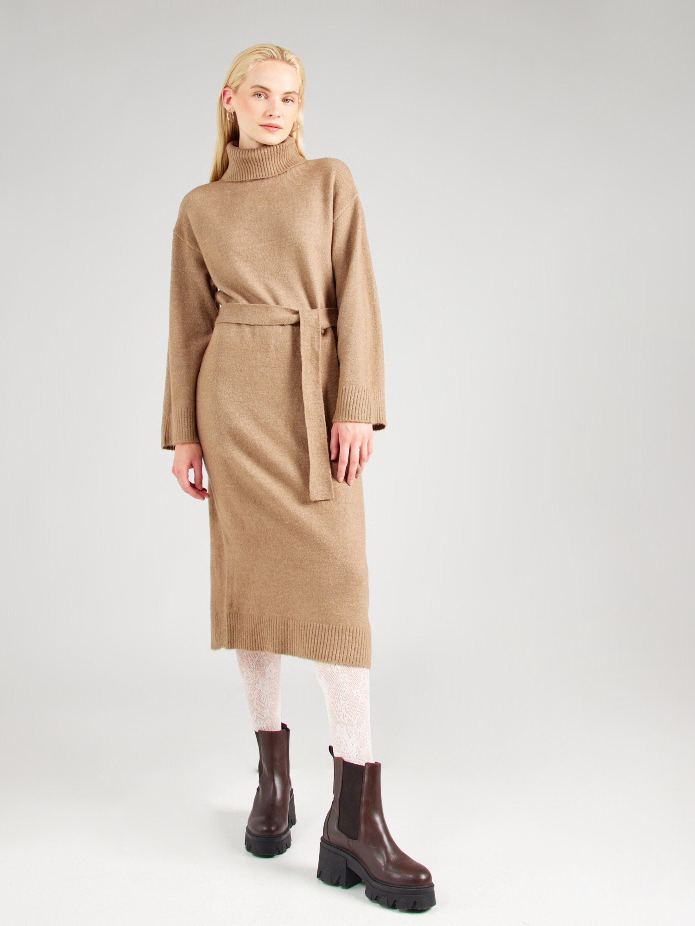 Woman in a camel sweater dress with white lace tights and brown lug Chelsea boots