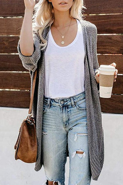 Woman in a gray open-knit cardigan, white tank top, ripped light-wash boyfriend jeans, tan crossbody bag holding a coffee