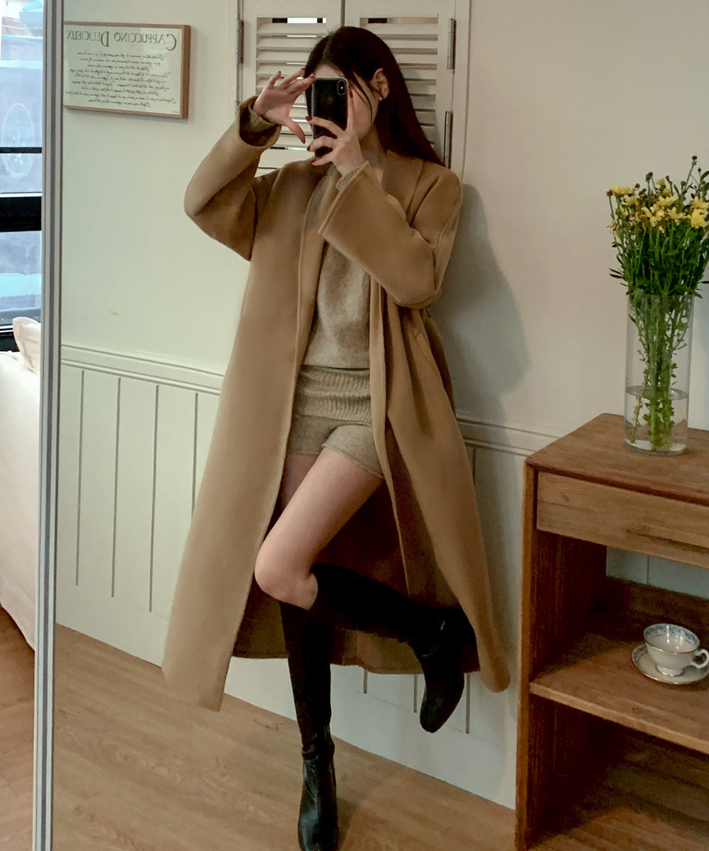 Woman in a camel wrap coat over a beige knit sweater and shorts with black knee-high boots