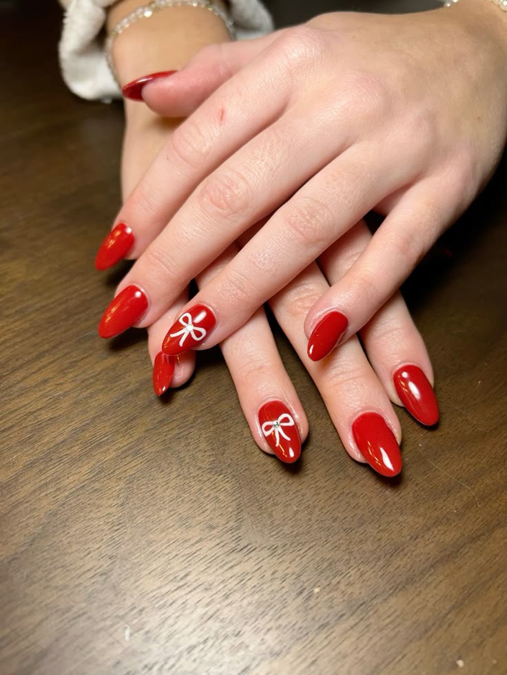 Glossy red almond nails with thin white hand-drawn bow outlines on two accent nails.