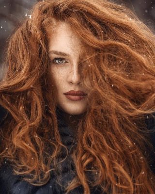 Voluminous fiery copper curls dusted with snow in a winter setting