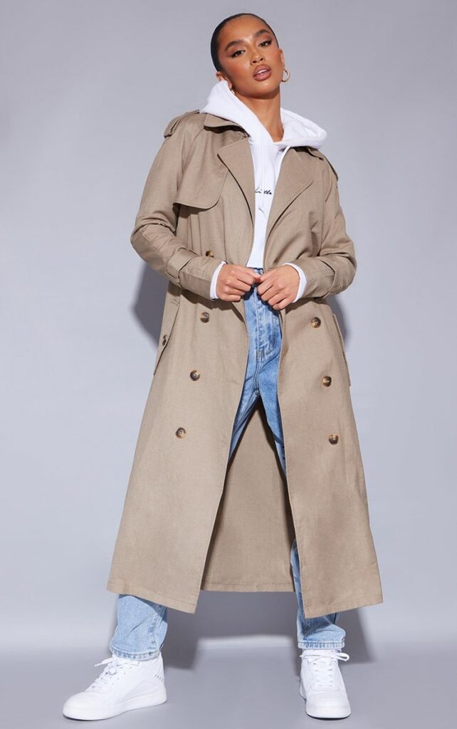 Woman in white hoodie under beige trench coat with jeans and white sneakers