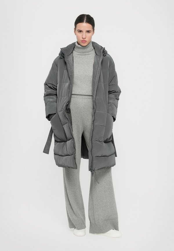 A woman wearing a long gray puffer coat with wide-leg trousers