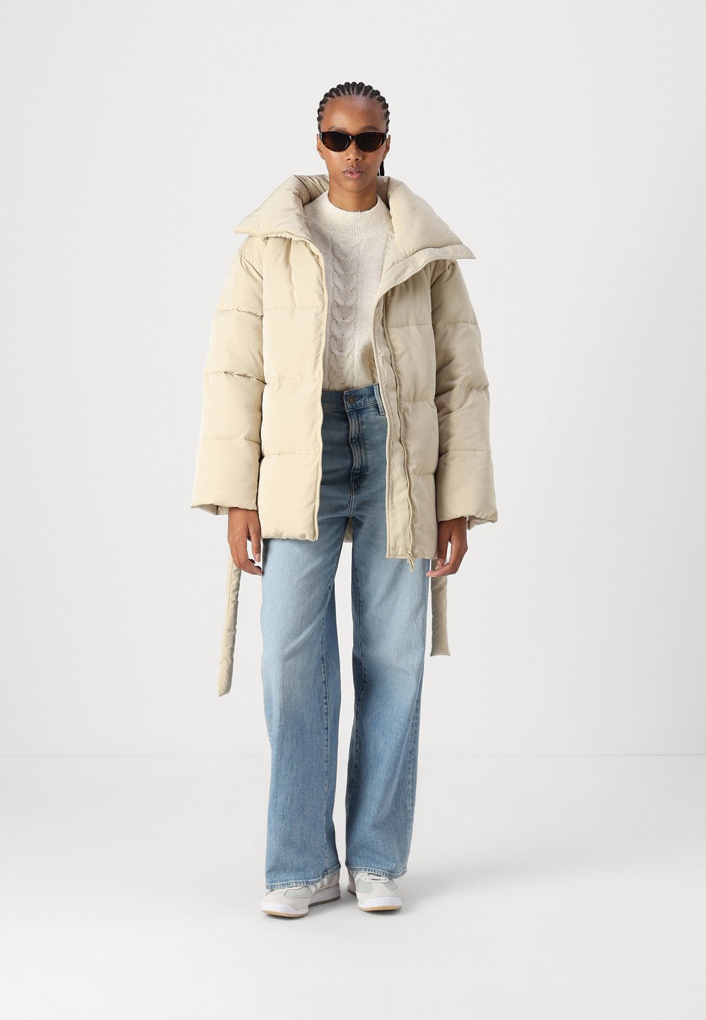 Woman in a beige quilted jacket with a cream sweater and jeans