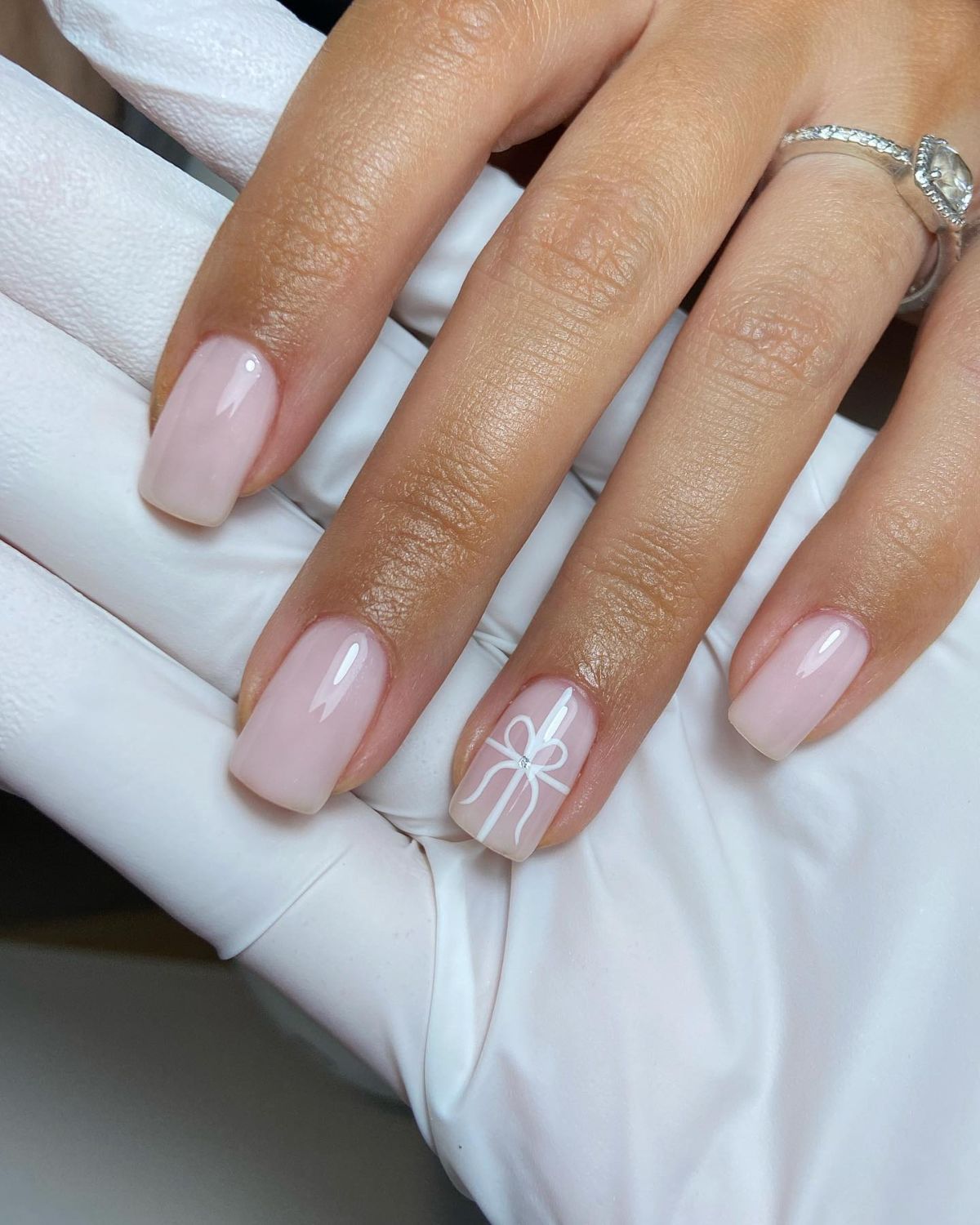 Nude nails with a tiny red bow accent on one nail
