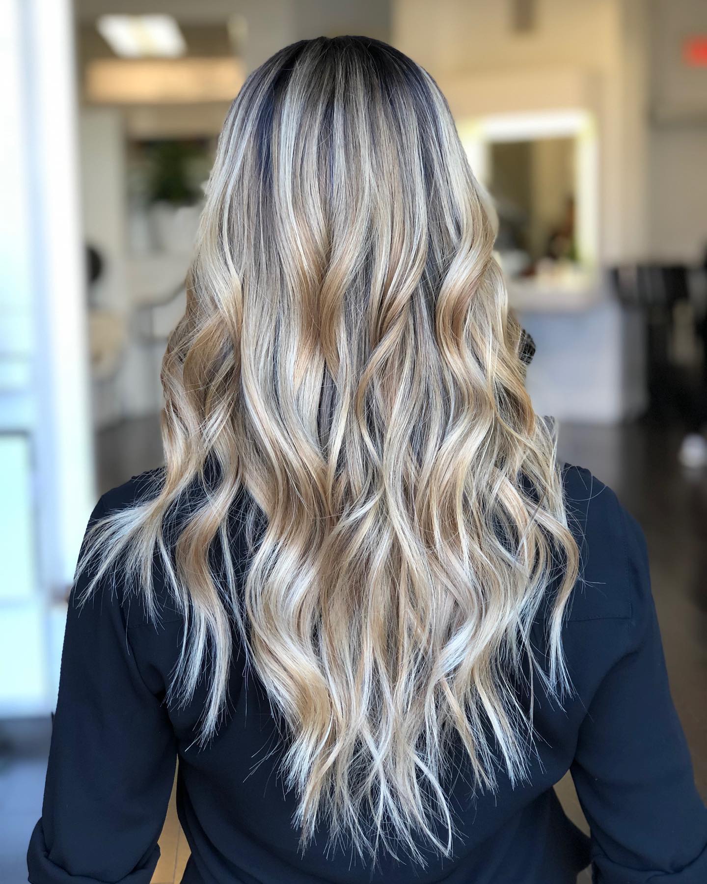 Back view of long wavy hair with dark shadow roots melting into bright ash-blonde balayage