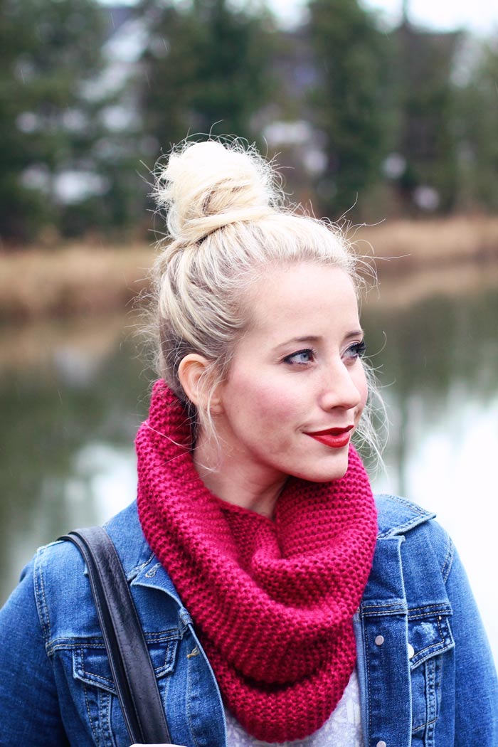Woman in a magenta chunky knit infinity scarf and denim jacket with her hair in a top bun