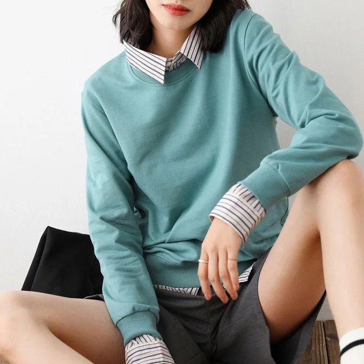 Woman wearing a teal sweatshirt layered over a striped collared shirt with gray shorts