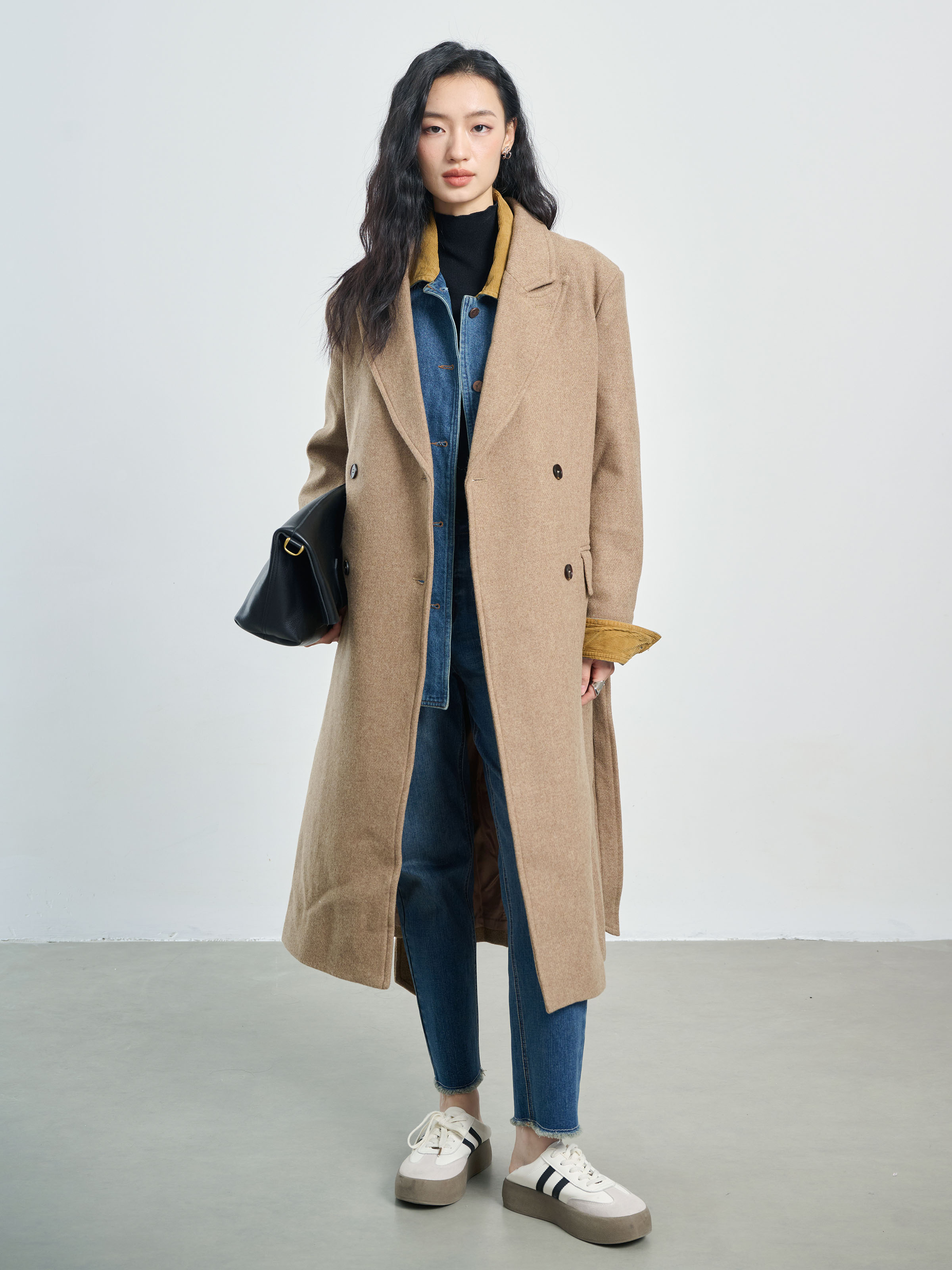 Woman in a camel wool coat over a black turtleneck and dark jeans