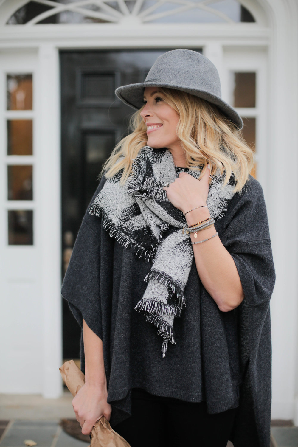 Woman in a grey felt hat, black and grey plaid fringed scarf and a dark poncho